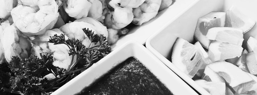 Black-and-white photograph of a shrimp platter with lemon wedges, parsley and dipping sauce